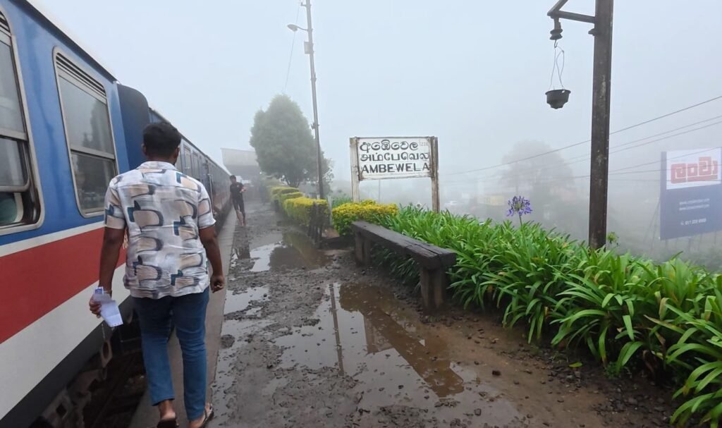 Ambewela station in thick morning fog, the train barely visible beside the platform sign.
