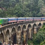 The blue train crossing Nine Arches Bridge, Ella in Sri Lanka's hill country, packed with tourists leaning from the open doorways.