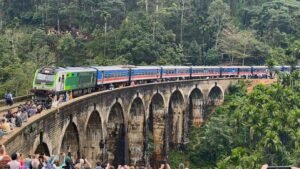 The blue train crossing Nine Arches Bridge, Ella in Sri Lanka's hill country, packed with tourists leaning from the open doorways.
