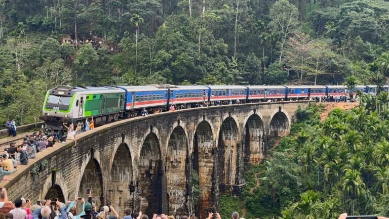 The blue train crossing Nine Arches Bridge, Ella in Sri Lanka's hill country, packed with tourists leaning from the open doorways.