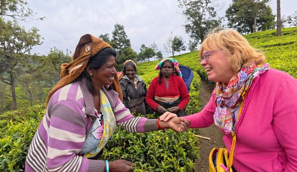 Mel talking with tea pickers among the bushes, the women carrying colourful baskets against the green hillside at Pedro Tea Estate, Nuwara Eliya.